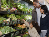 A photo of a young family of colour, selecting vegetables at the supermarket.