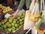 A photo of a woman holding a string bag, gathering citrus fruit and putting it in the bag