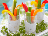 Three glasses filled with a low fat dip and vegetable sticks, including celery and red and yellow peppers